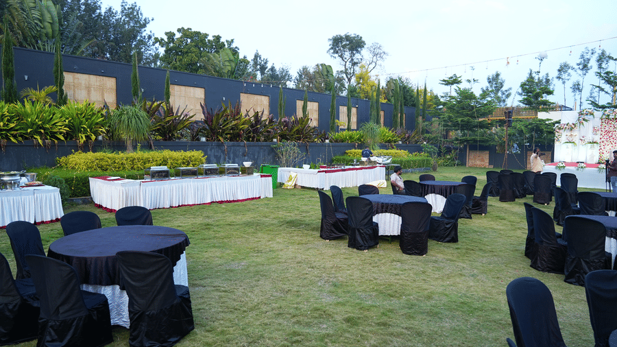 An outdoor event setup with small, black clothed tables and matching chairs arranged on a grassy area, backed by a modern hotel exterior and landscaping at Bindiga Peak Resorts.