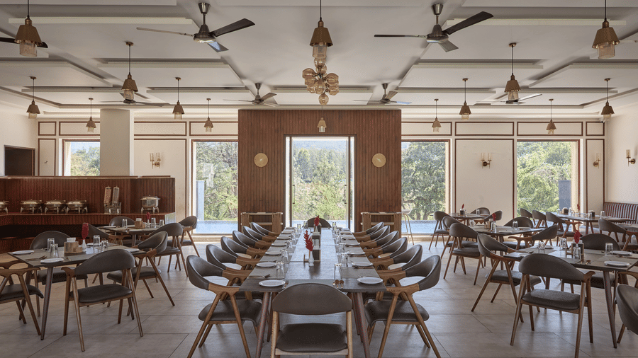 Spacious, modern dining hall with rows of tables, brown chairs, rectangular ceiling panels, and brass light fixtures at Bindiga Peak Resorts.
