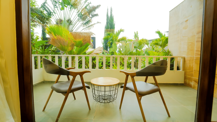 A balcony with two brown chairs and a wire-frame table looking out towards green trees at Bindiga Peak Resort.
