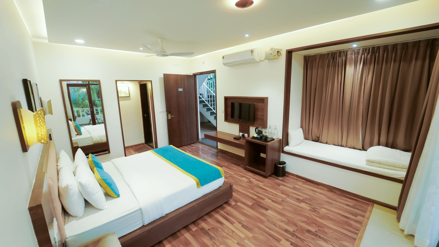 A room at Bindiga Peak Resort featuring a large bed with a blue runner, a wall-mounted television, and a window along with brown curtains.