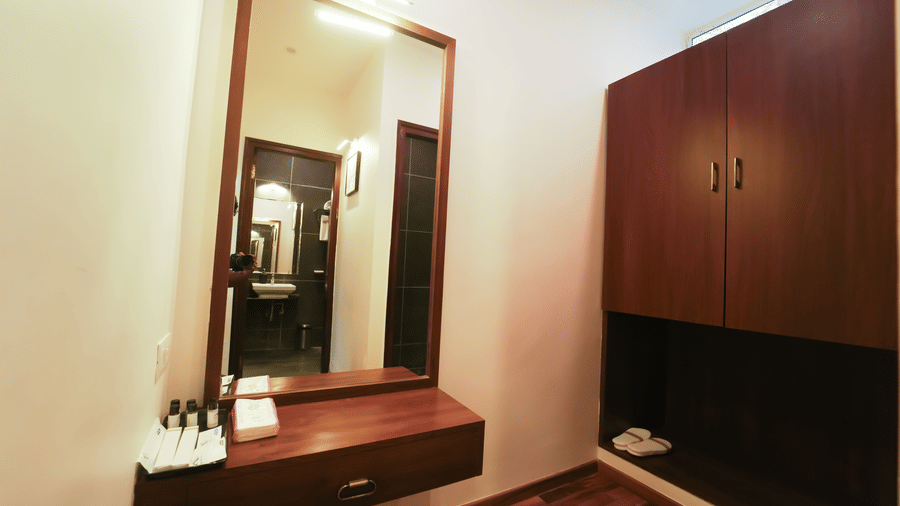 A vanity space with a large wall mirror, a wooden floating drawer, and a tall wooden wardrobe at Bindiga Peak Resort.