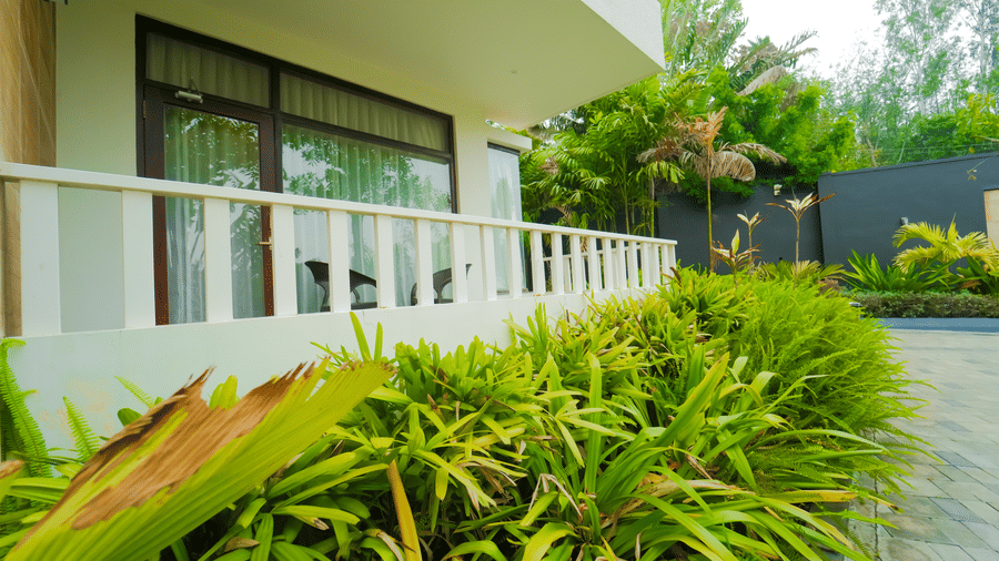 A building at Bindiga Peak Resort with a white railing balcony positioned behind thick green bushes.