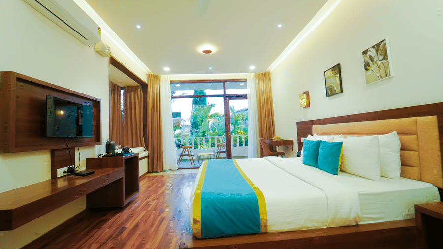 A bedroom with a large bed, a wall-mounted television, and glass doors opening to a balcony at Bindiga Peak Resort.