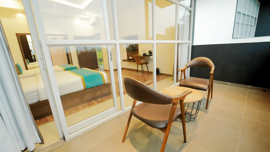 Sitting area in the balcony of the executive Suite at Bindiga Peak Resort with 2 wooden chairs and a table next to a large glass door showing the bedroom.
