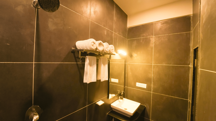 A bathroom at Bindiga Peak Resort featuring dark grey wall tiles, a shower head, stacked white towels, and a white sink.