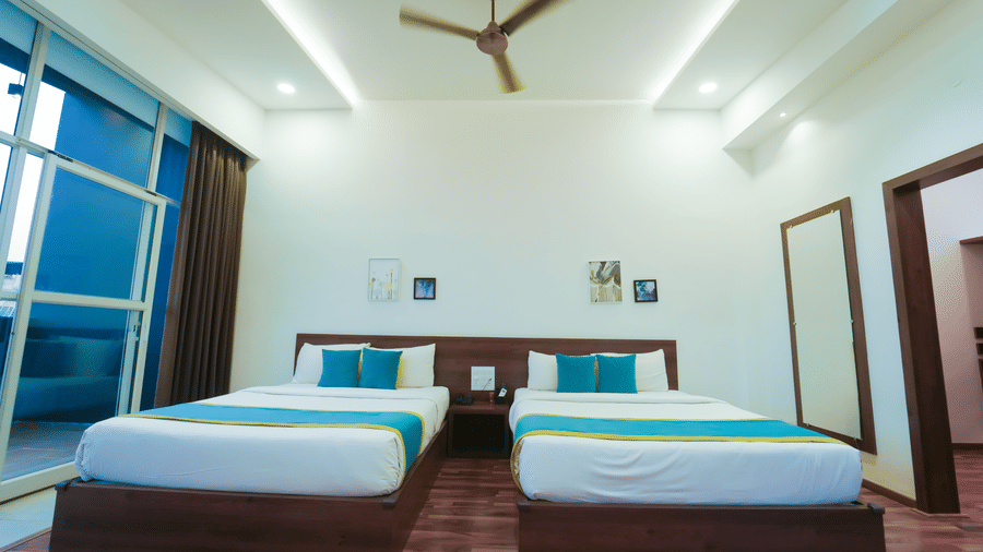 A bedroom at Bindiga Peak Resort with 2 beds, white walls, a balcony, and ceiling fan.