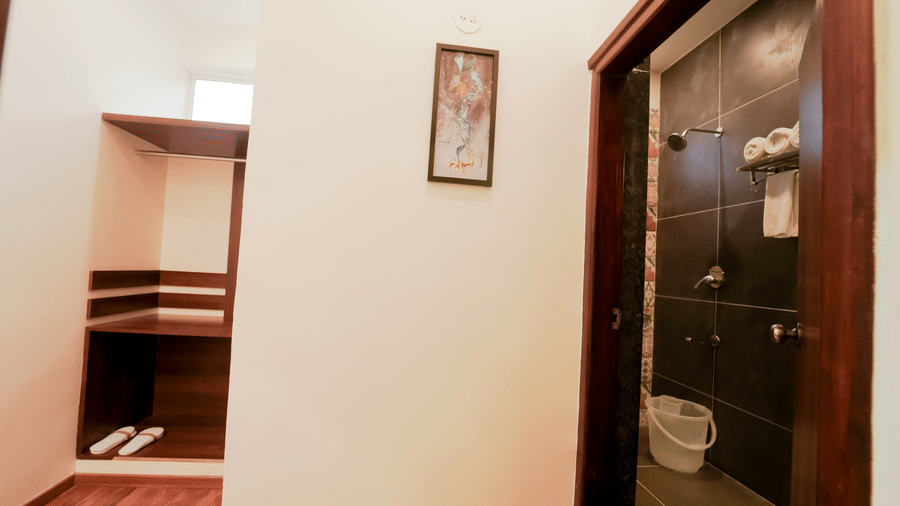 Interiors of a room at Bindiga Peak Resort with white walls, a wooden closet area, and an open doorway leading into a bathroom.