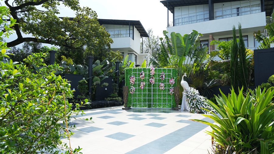 An outdoor chequered-tiled patio with green decorative panels and floral arrangements next to white villas at Bindiga Peak Resort.