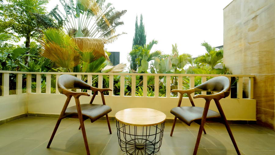 A balcony at Bindiga Peak Resort with 2 wooden chairs, a wire-frame coffee table, and a white railing.