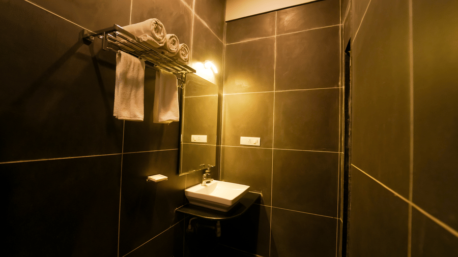 A bathroom at Bindiga Peak Resort with dark grey wall tiles, a square white washbasin, a mirror, and a towel rack with white towels.