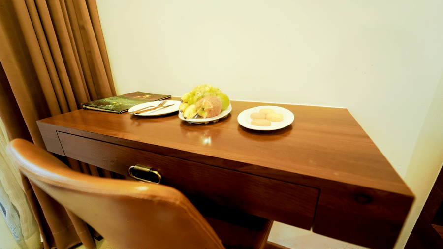 A room with a wooden desk with a brown chair, white plates with food, and brown curtains at Bindiga Peak Resort.