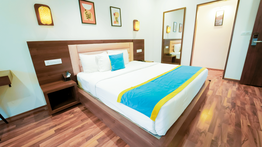 A bedroom at Bindiga Peak Resort with a large bed, white bedding with a teal and yellow runner, wooden flooring, and framed art on the wall.