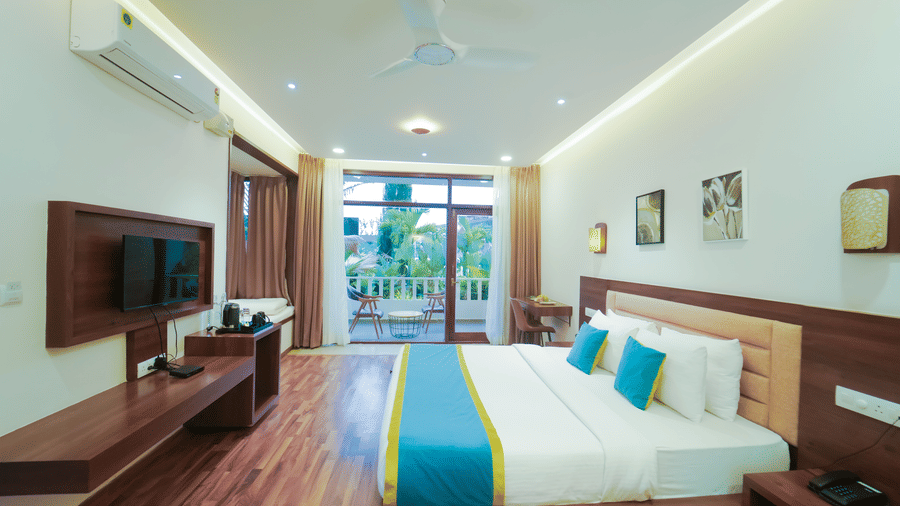 Room at Bindiga Peak Resort featuring a bed, a wall-mounted television, wooden floor, and a glass door leading out to a balcony.