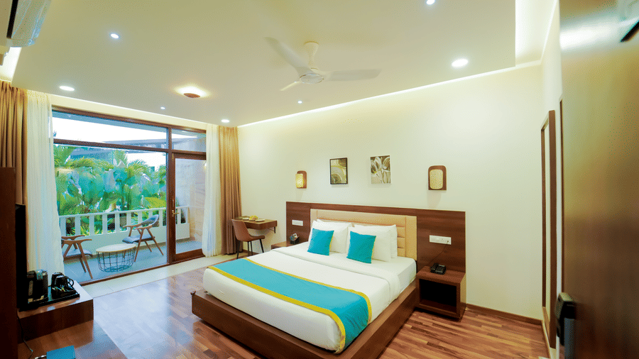 A bedroom at Bindiga Peak Resort with a large bed, wooden flooring, and large glass doors that open to an outdoor balcony.