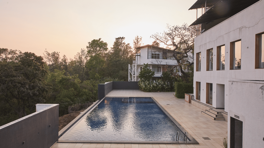 A rectangular outdoor swimming pool running alongside white resort buildings and a concrete wall under a light sky at Bindiga Peak Resort.