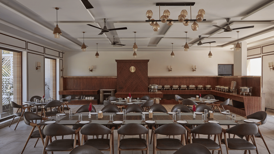 A restaurant dining area featuring wooden table, chairs, multiple ceiling fans and buffet counters at Bindiga Peak Resort.