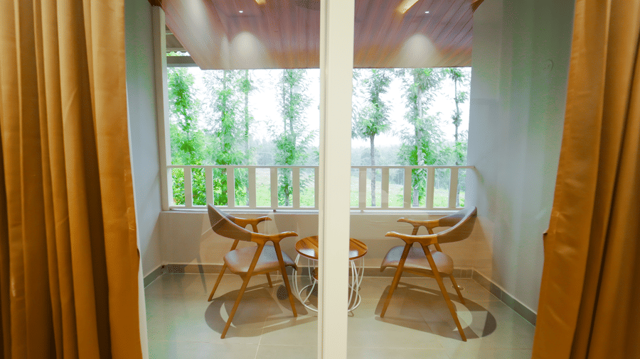 Glass doors with brown curtains that leads to the balcony with 2 chairs and a round table at Bindiga Peak Resort