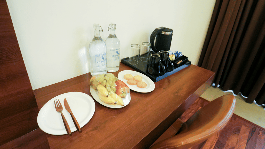 A wooden desk with plates, water bottles, and an electric kettle next to brown curtains at Bindiga Peak Resort.