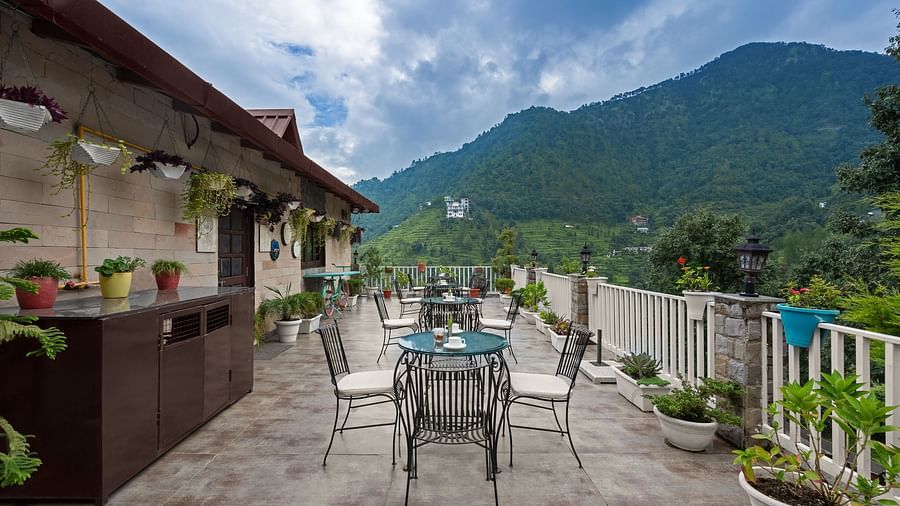Rooftop dining area with mountain views under a cloudy blue sky, at BluSalzz Collection - Suvaasa Resort, Ramgarh.