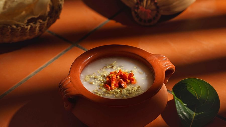 A close-up of a clay pot filled with a creamy dish, garnished with spices and herbs.