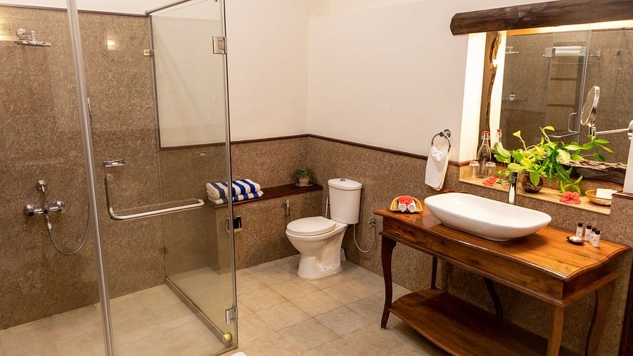 Bathroom with a glass shower, white sink on a wooden stand, and a window - BluSalzz Collection - Tranquil Resort, Wayanad
