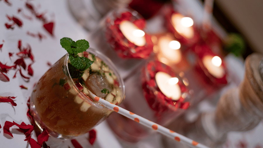 A glass with a beverage and a straw sits on a surface decorated with flower petals and candles at BluSalzz Escapade Resort, Lansdowne.
