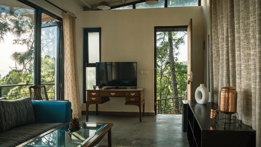 A seating area in the Pine Forest Suite includes a sofa, a coffee table, and a television on a console. Windows and a door lead outside.