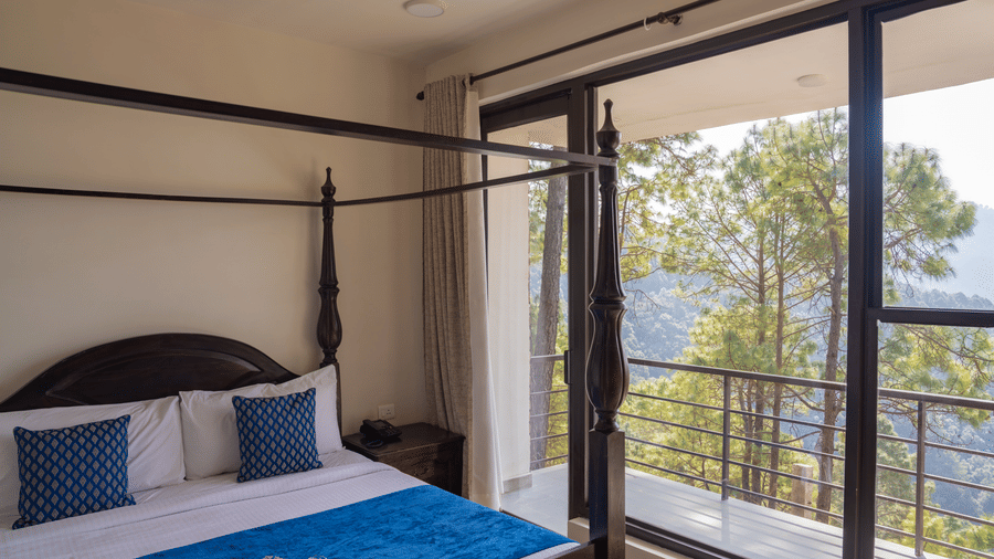 A four-poster bed stands next to large glass windows in the Pine Forest Suite. The windows look out onto hills and pine trees.