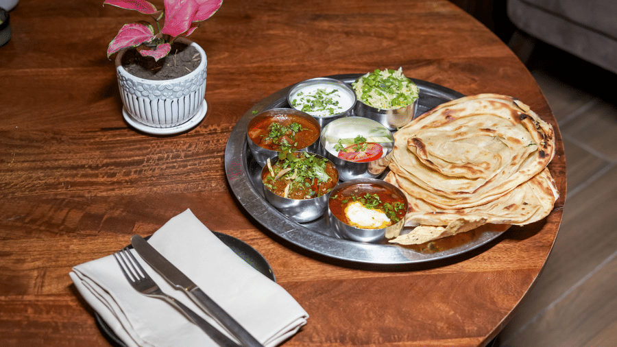 A metal thali platter with various curries and side dishes, served next to a stack of flatbreads or parathas at BluSalzz Select City Centre, Amritsar.