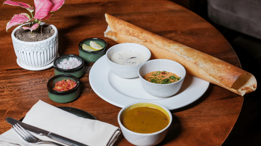 A crisp, rolled dosa served on a wooden table with sambar, chutney, and other small side dishes at BluSalzz Select City Centre, Amritsar.