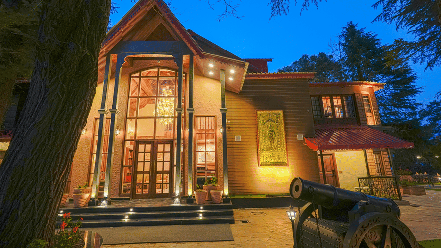 The well-lit facade of BluSalzz Terrah Hills Resort, Dalhousie, with steps in the entrance, a large wooden door, and trees in the backdrop at night.