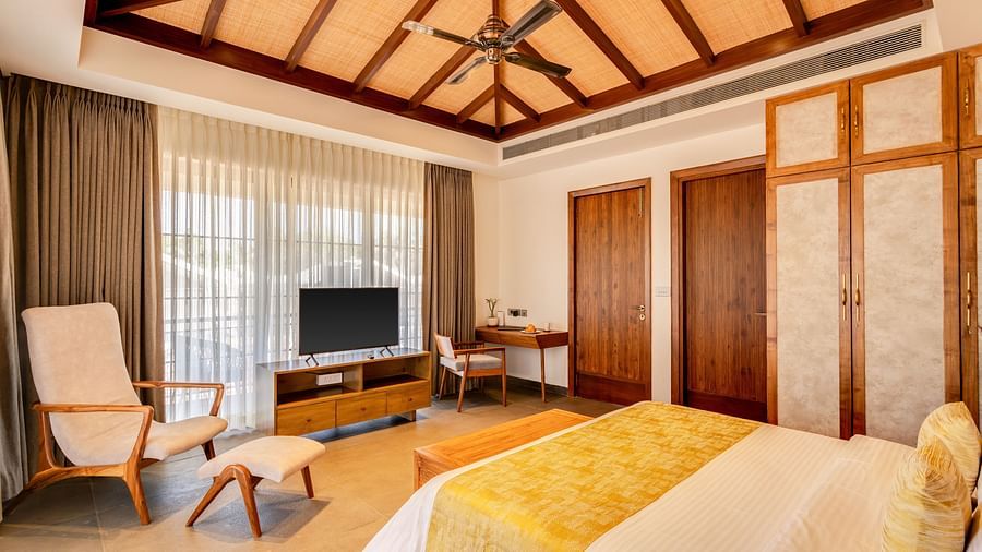 A luxurious bedroom with a pitched wooden ceiling, a seating area, and a comfortable bed adorned with soft yellow decor - BluSalzz Villas - Alocassia, Anjuna
