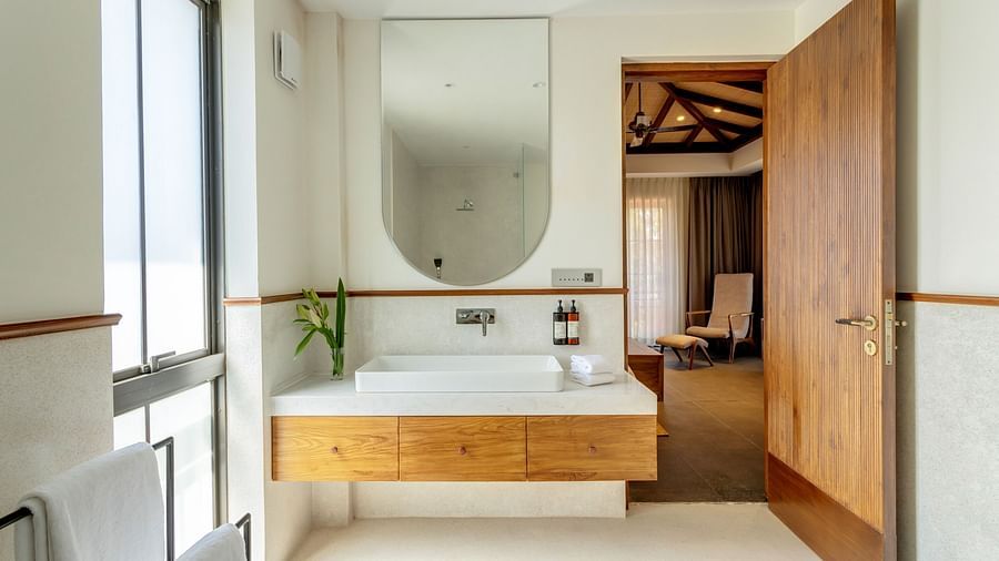 A sleek bathroom with a wooden vanity, a round mirror, and natural light streaming in through the large window - BluSalzz Villas - Alocassia, Anjuna