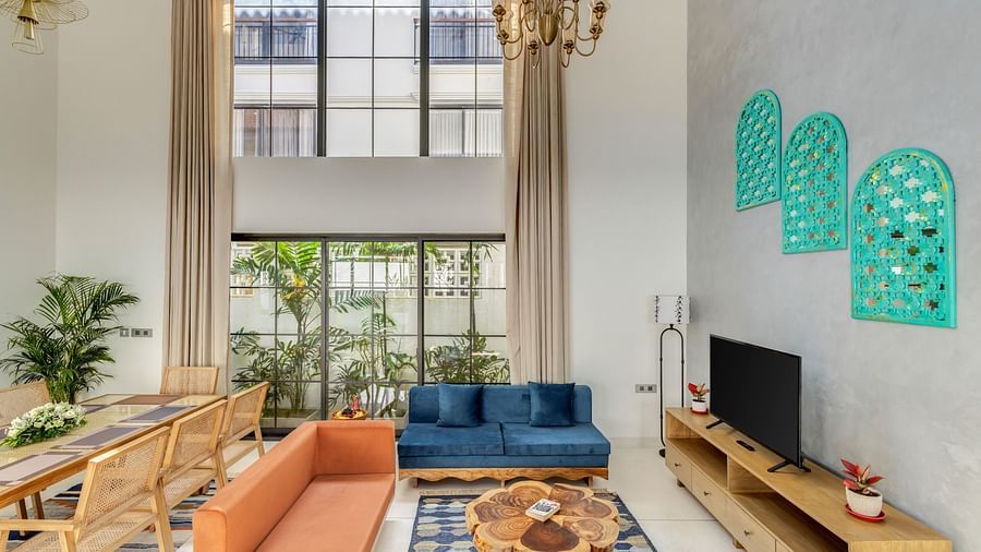 A vibrant open living area with high ceilings, large windows, and stylish wooden furniture arranged for comfort - BluSalzz Villas - Alocassia, Anjuna