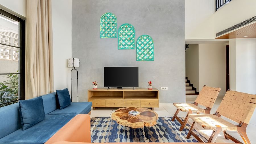 A contemporary living room featuring a blue sofa, orange armchairs, a wooden coffee table, and artistic green wall decor - BluSalzz Villas - Alocassia, Anjuna
