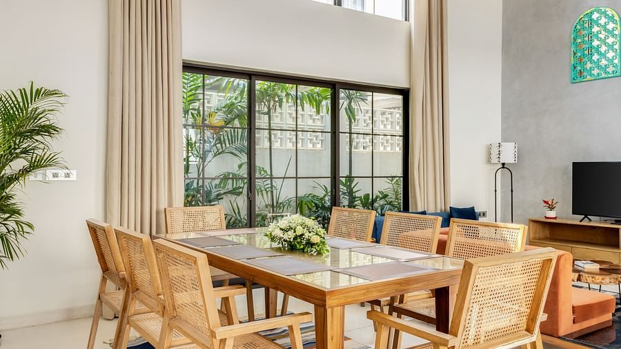 A dining area with a contemporary wooden table, modern chairs, and large windows bringing in natural light - BluSalzz Villas - Alocassia, Anjuna
