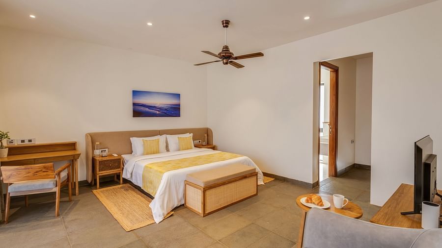 A wide-angle view of a bedroom with a double bed, a work desk, and a door leading to a private balcony - BluSalzz Villas - Alocassia, Anjuna