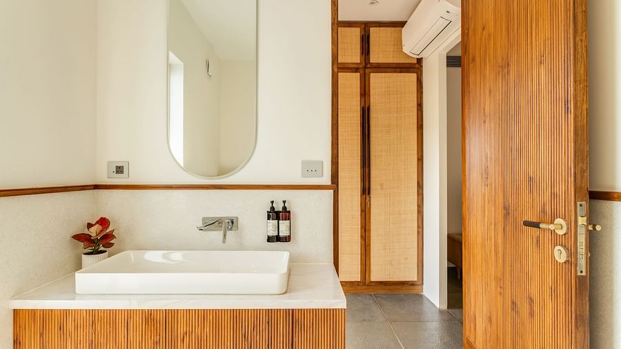 A bathroom with a wooden vanity, rectangular mirror, and a combination of natural and artificial lighting creating a cosy atmosphere - BluSalzz Villas - Alocassia, Anjuna