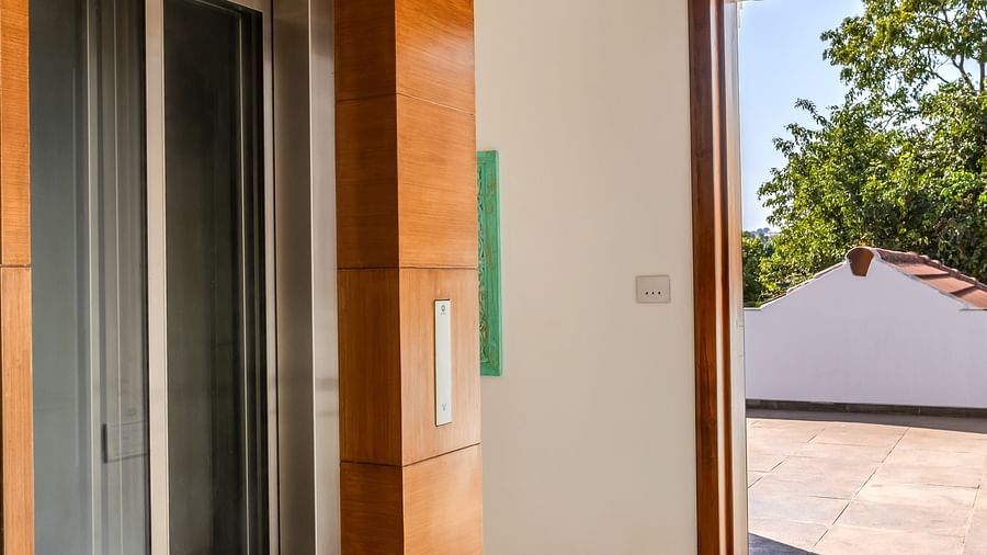 A corridor with wooden accents leading to a glass door that opens to an outdoor area under a clear blue sky - BluSalzz Villas - Alocassia, Anjuna