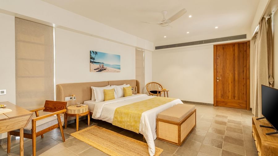 A spacious bedroom with a neatly made double bed, a work desk, and a television, complemented by soft yellow and beige decor - BluSalzz Villas - Alocassia, Anjuna