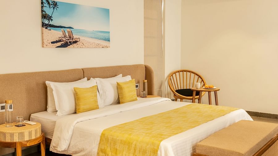 A cosy bedroom with a comfortable bed adorned with yellow cushions, a beach-themed artwork, and wooden accents - BluSalzz Villas - Alocassia, Anjuna