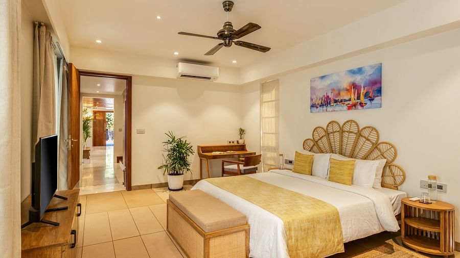 A wide-angle view of a bedroom with a king-sized bed, vibrant artwork, and wooden accents, creating a warm and inviting atmosphere - BluSalzz Villas - Alocassia, Anjuna