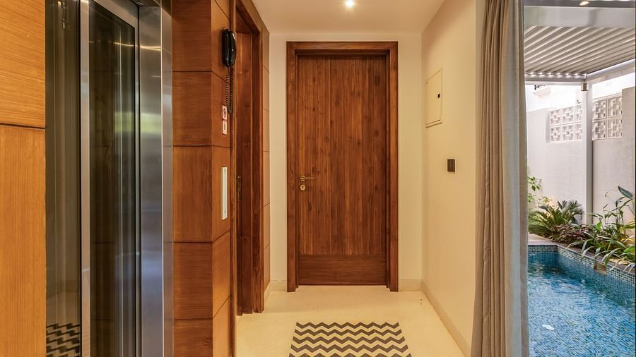 A wooden entrance door with intricate detailing, leading to a modern interior with patterned flooring - BluSalzz Villas - Alocassia, Anjuna