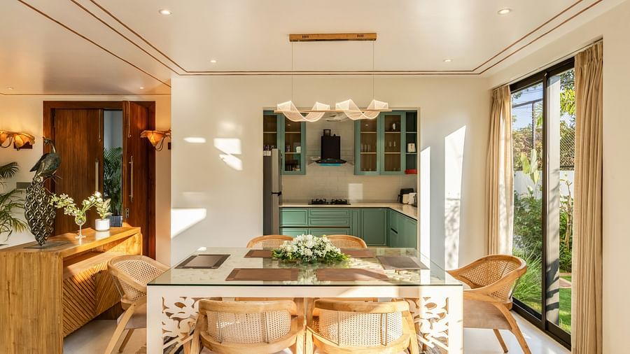 A dining area with a wooden table and chairs, complemented by natural light and an open-plan design connected to the kitchen - BluSalzz Villas - Alocassia, Anjuna