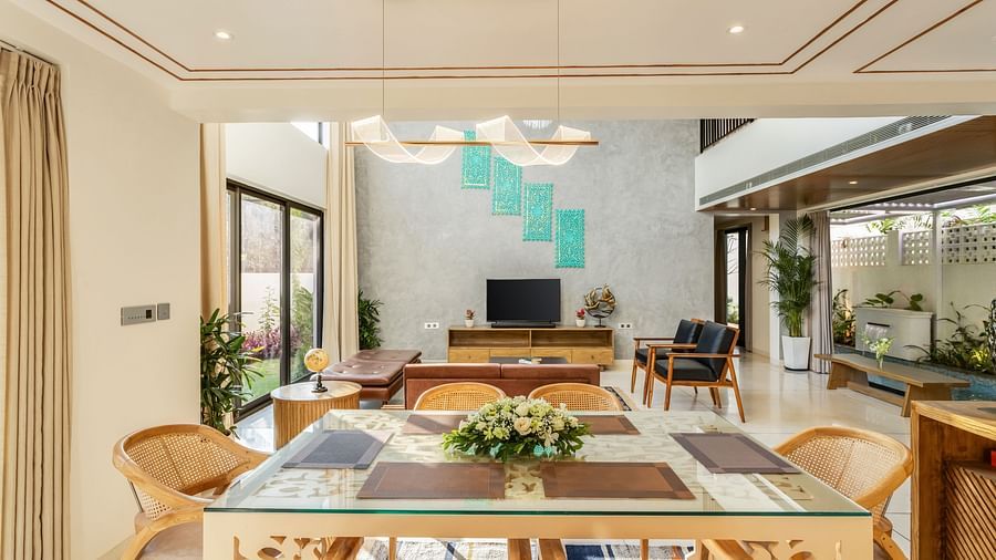 A dining area with a wooden table, modern chairs, and large windows offering views of the living room and outdoor greenery - BluSalzz Villas - Alocassia, Anjuna