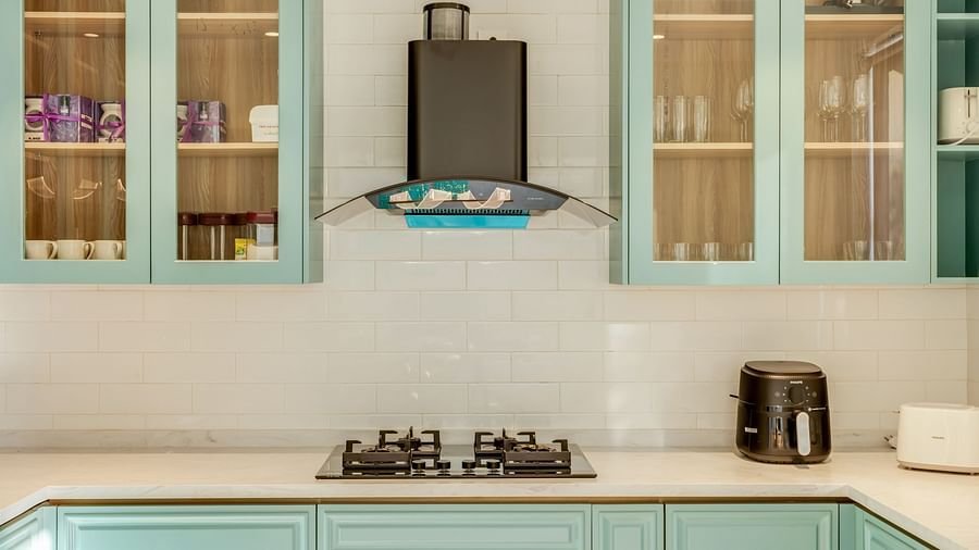 A modern kitchen with pastel blue cabinets, a sleek stovetop, glass-fronted shelves, and minimalistic decor - v