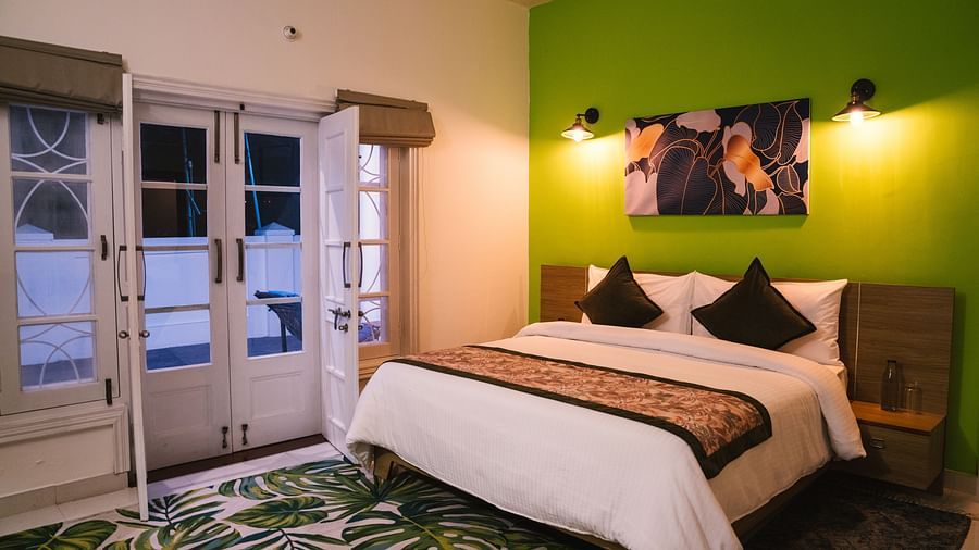 A spacious room at BluSalzz Villas - The Green Roof, Bhimtal, featuring a large bed with a photo frame above the headboard, night lamps glowing on either side, a carpet, and a door leading to the balcony.