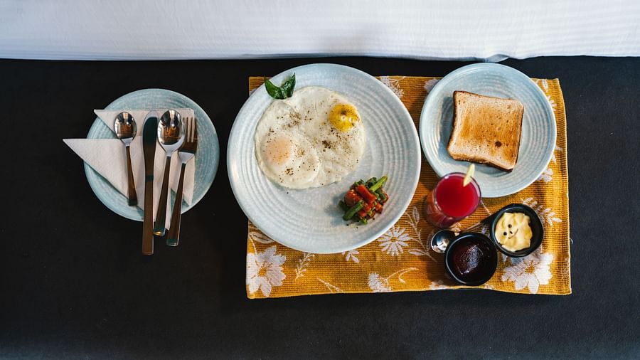 A top view of three plates at BluSalzz Villas - The Green Roof, Bhimtal, featuring toast, an omelette with vegetables, and cutlery alongside jam, butter, and a lit candle.
