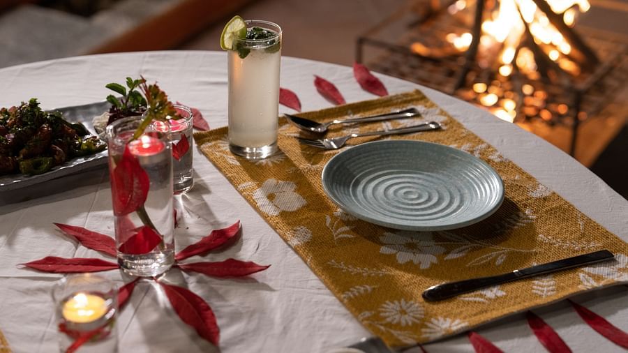 A close-up view of a table neatly set with food and cutlery, with a campfire in the background at BluSalzz Villas - The Green Roof, Bhimtal.