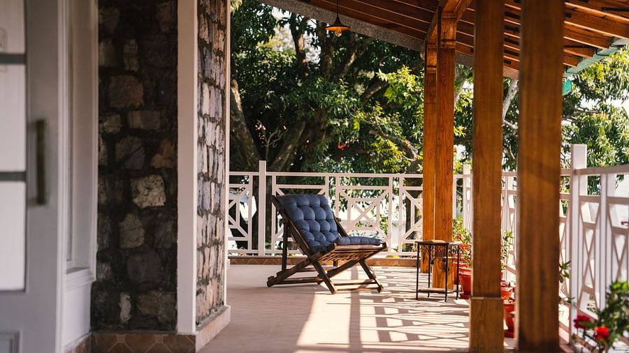 A foldable chair placed on the porch, framed by the stone wall and wooden pillars at BluSalzz Villas - The Green Roof, Bhimtal.